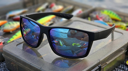Lunettes polarisantes à miroir bleu et monture noire mate posées sur le couvercle d'une boîte à leurres ouverte, leurres colorés autour
